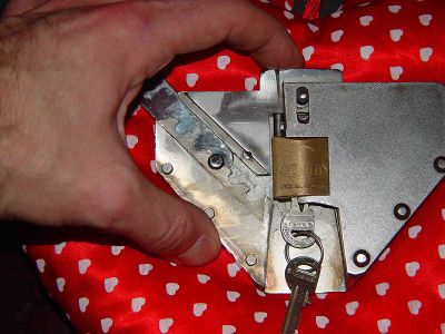 21. By pushing on the upper extension of the locking block the groove, with the knob of the waistbelt hooked in, will close. At once the hidden shackle of the padlock is pinned into its gold case